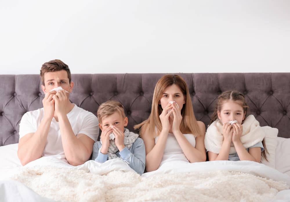 Young family all holding tissues on their nose while laying in bed