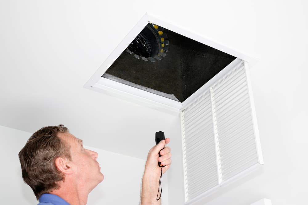 a technician using a flashlight while checking an air duct vent
